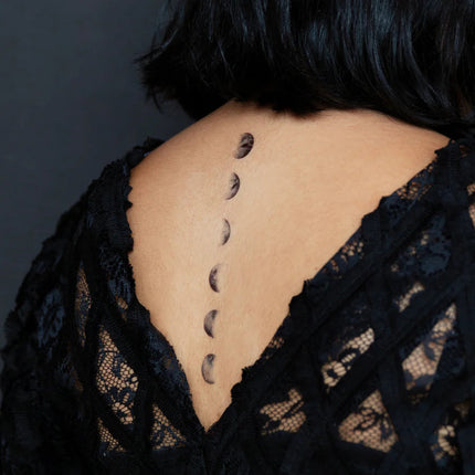 a slight side angle of a model's upper back showing the moon phase tattoos laid out in a delicate line following her spine
