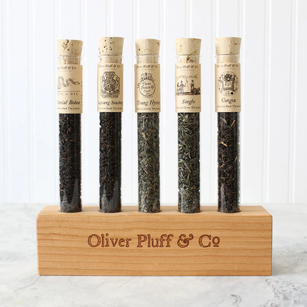 Five tea samples in test tubes with cork lids on a wooden stand, branded 'Oliver Pluff & Co'.