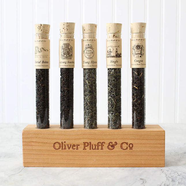 Five tea samples in test tubes with cork lids on a wooden stand, branded 'Oliver Pluff & Co'.