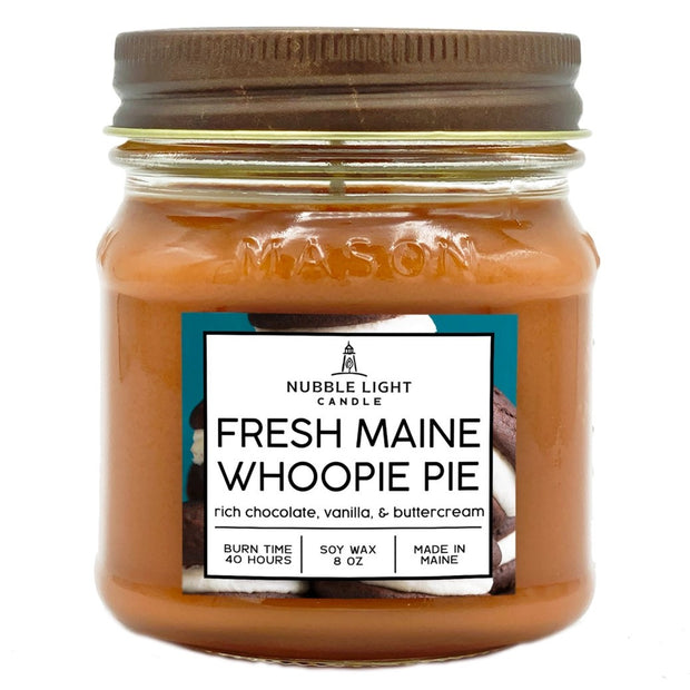 a candle in a clear glass mason jar with light brow wax and a label that reads "Maine Whoopie Pie" against a white background